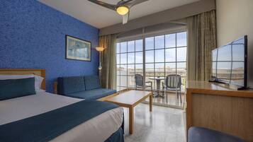 A hotel room with a bed, a sofa, a desk, a TV, and a balcony with a view.