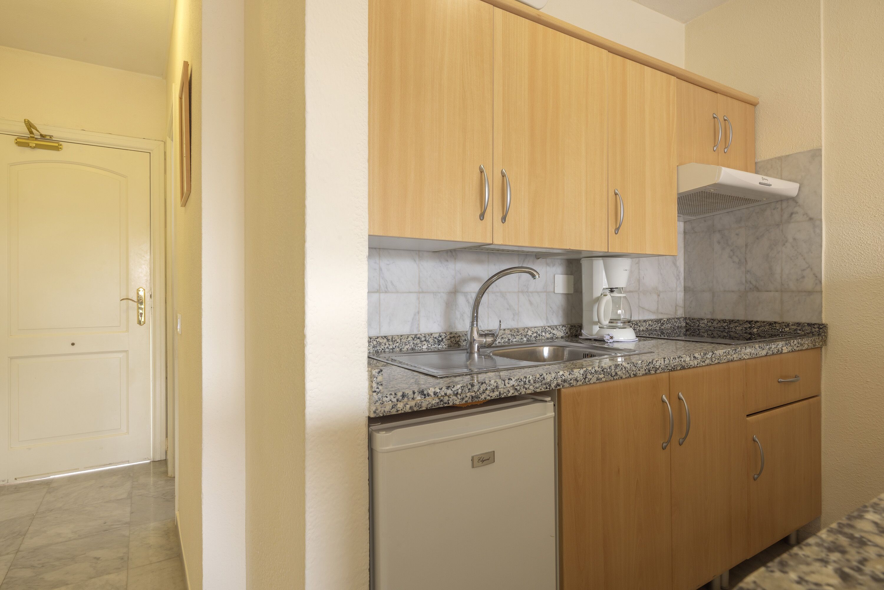 A kitchen with wooden cabinets, a stainless steel sink, a coffee maker, and a white refrigerator.