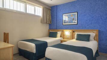 Habitación de hotel con dos camas, un escritorio, una silla, ventilador de techo, ventana con cortinas y un cuadro en la pared.