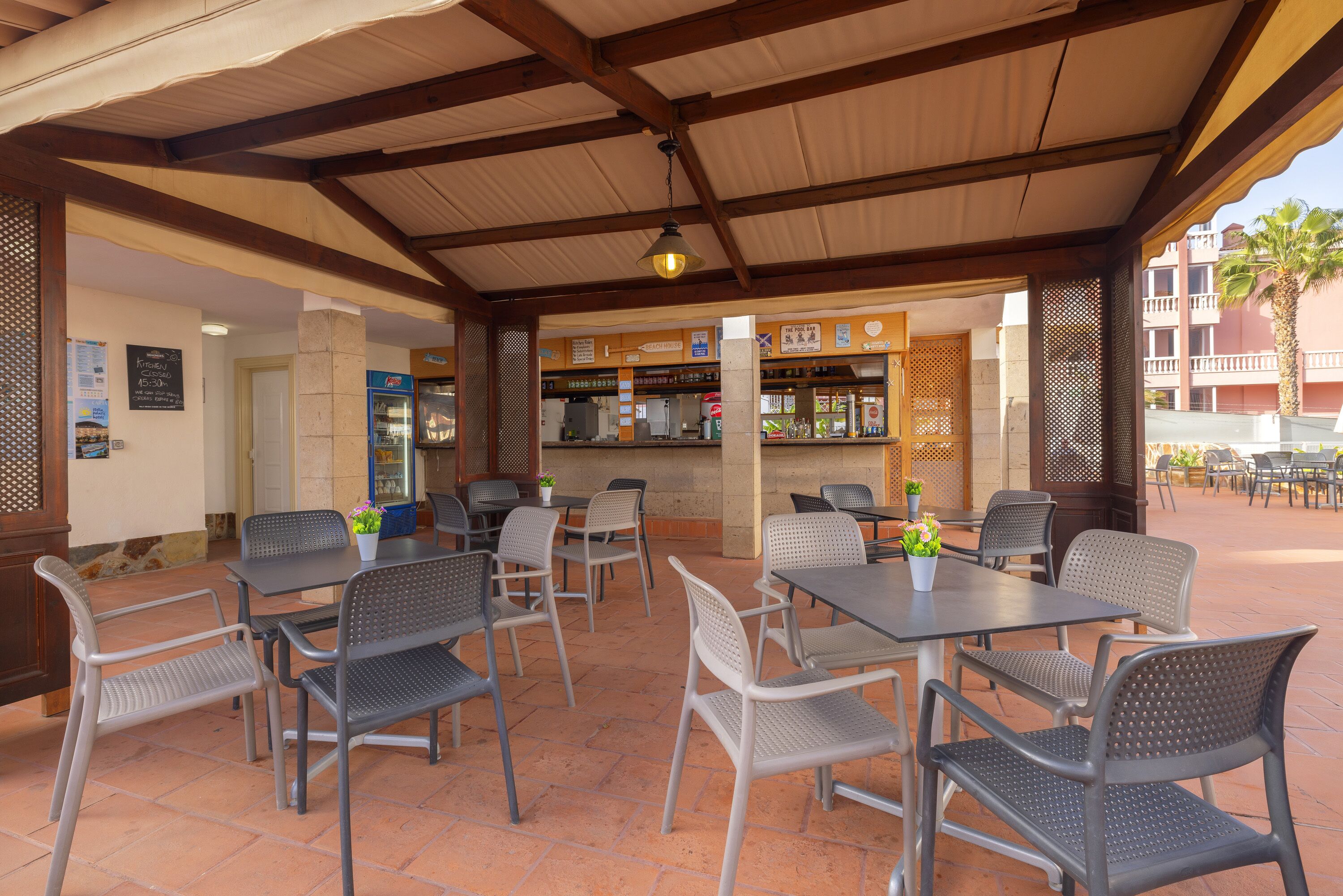 An outdoor patio area with tables and chairs, a bar, and a view of a building with balconies.