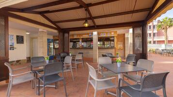 An outdoor patio area with tables and chairs, a bar, and a view of a building with balconies.