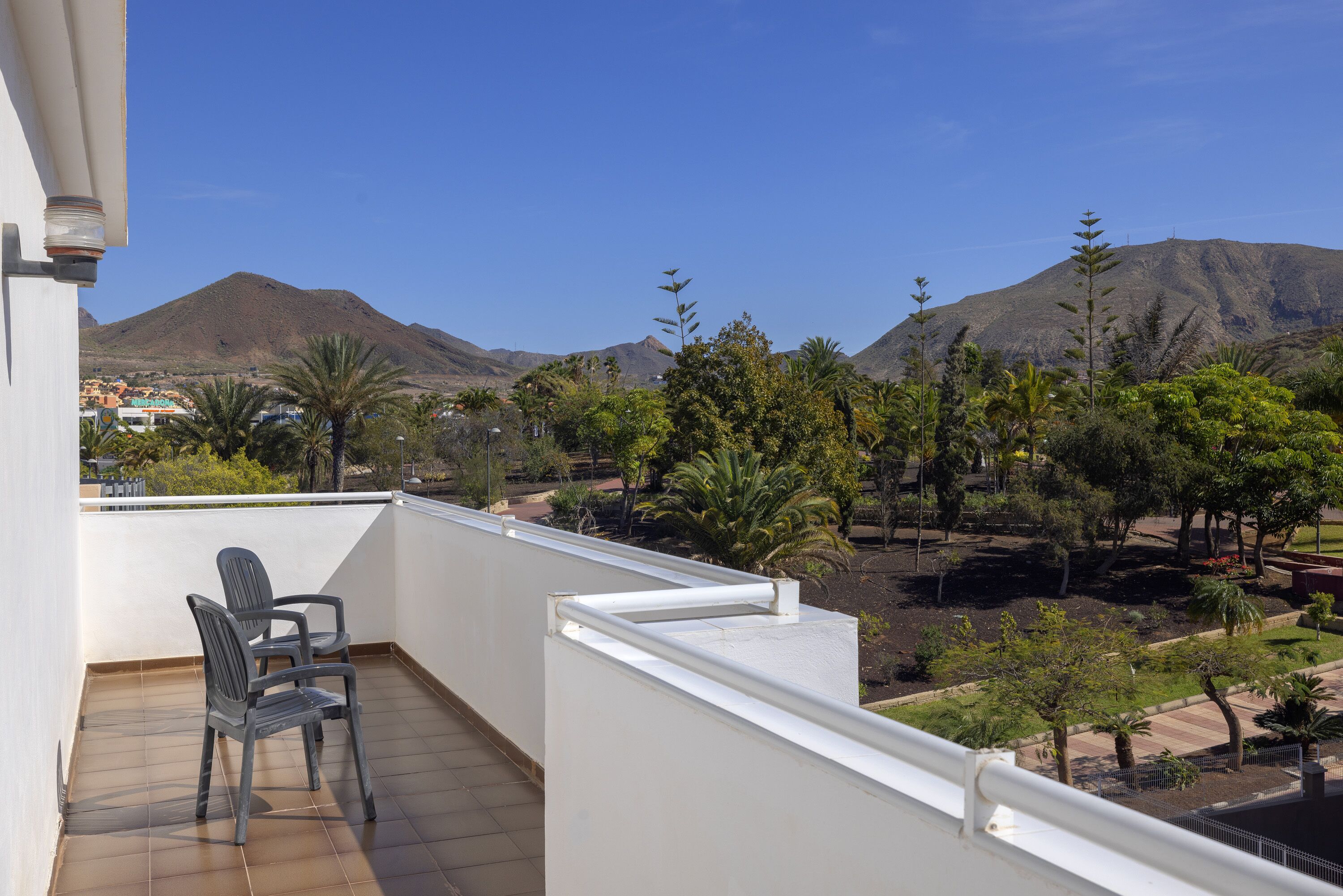 Un balcón con dos sillas, vistas a montañas y un jardín con diversas plantas.