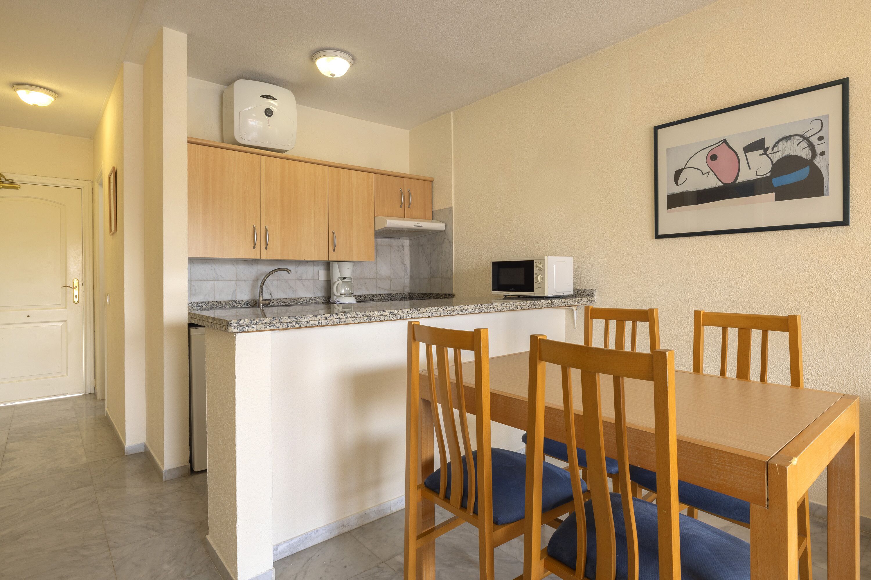 Una cocina compacta con armarios de madera, encimera de granito y un comedor con sillas y mesa de madera.