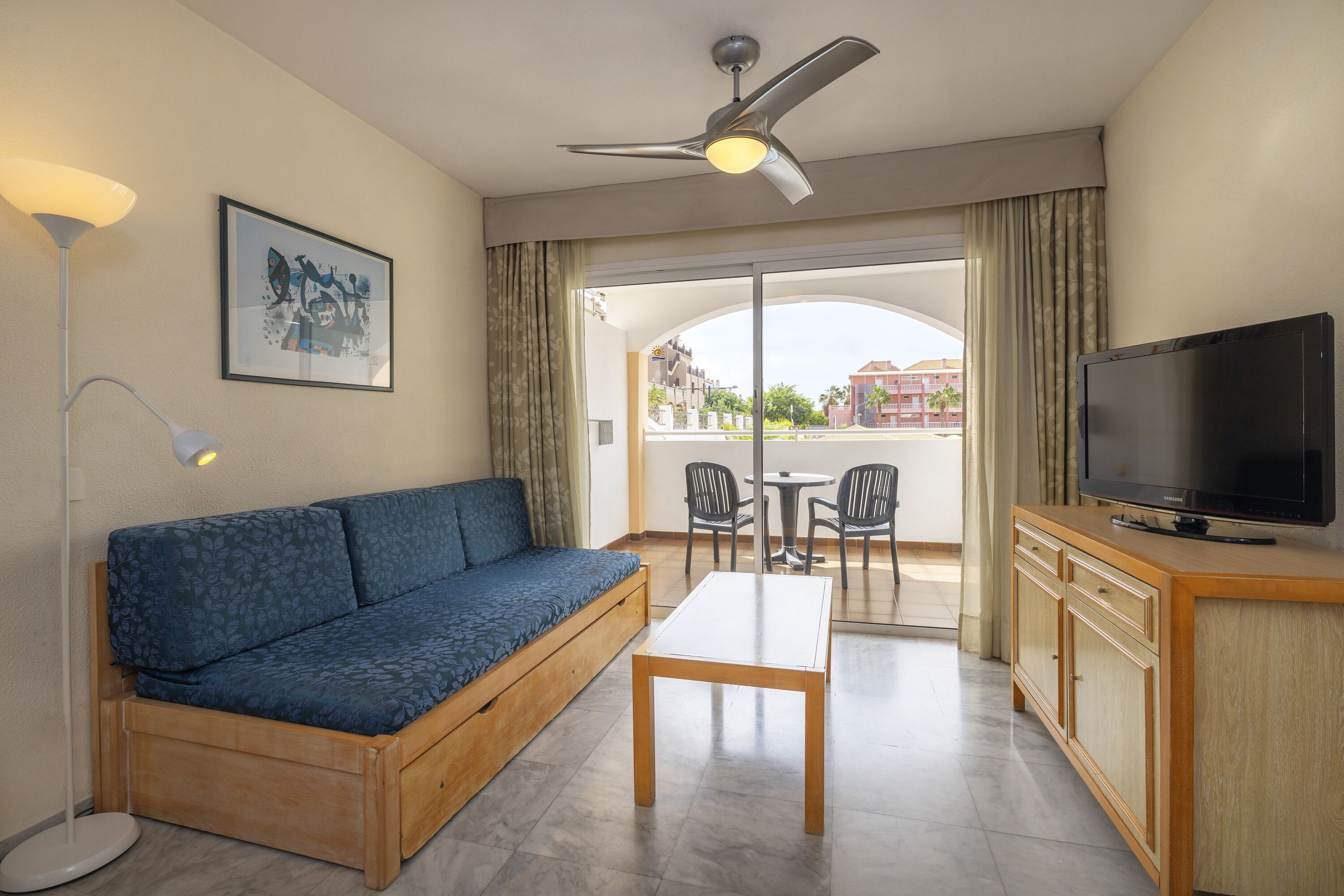 A room with a sofa, a table, a TV, and a ceiling fan.