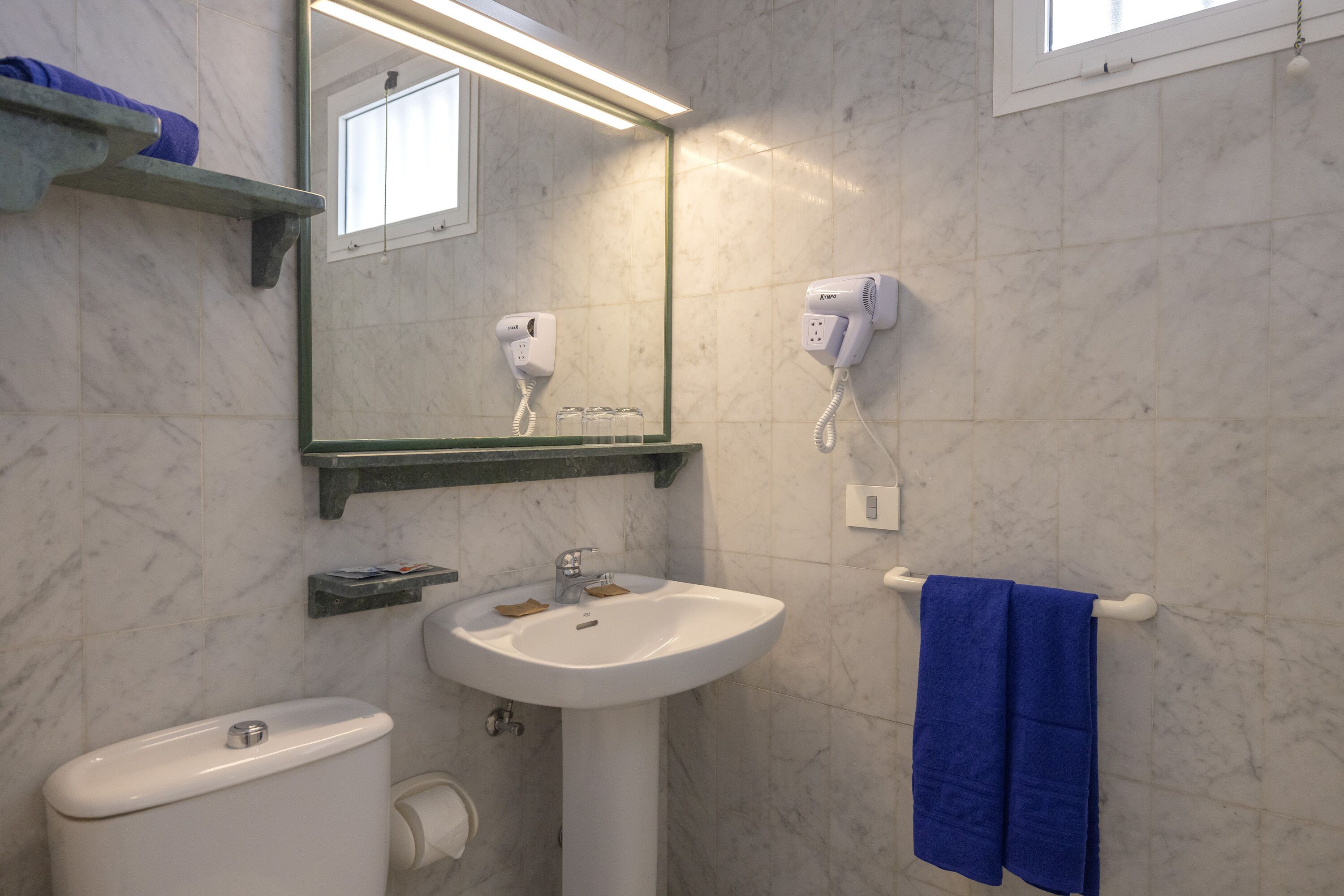 Une salle de bain avec un lavabo blanc, un miroir, un sèche-cheveux et un porte-serviettes.