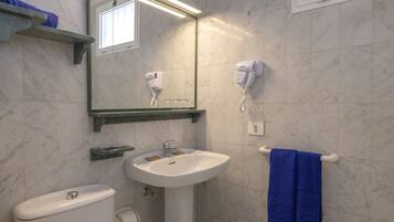 Une salle de bain avec un lavabo blanc, un miroir, un sèche-cheveux et un porte-serviettes.