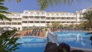 A hotel with a large swimming pool, multiple balconies, and sun loungers.