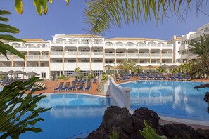 A hotel with a large swimming pool, multiple balconies, and sun loungers. - whala!tenerife (Arona)