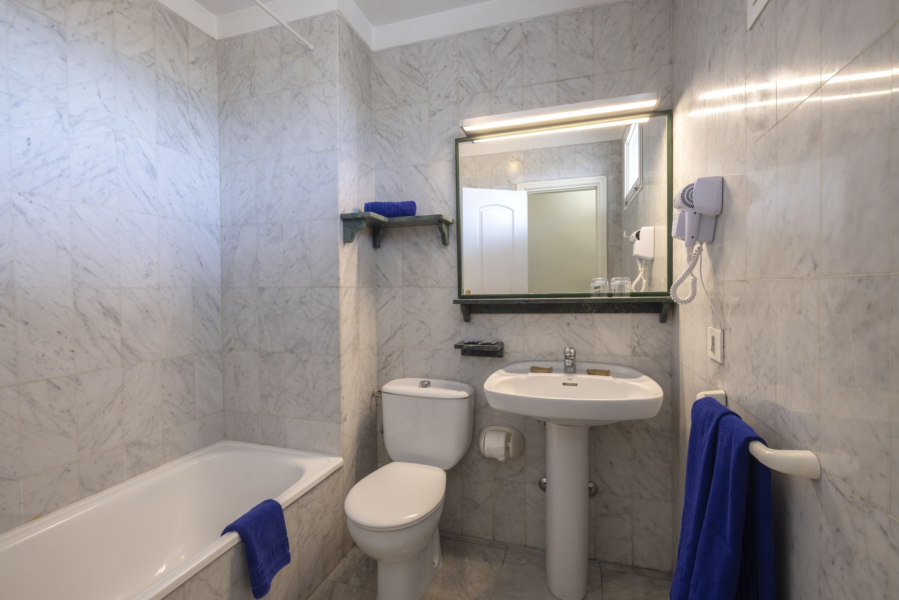 Un baño con bañera, inodoro, lavamanos y un secador de pelo en la pared.