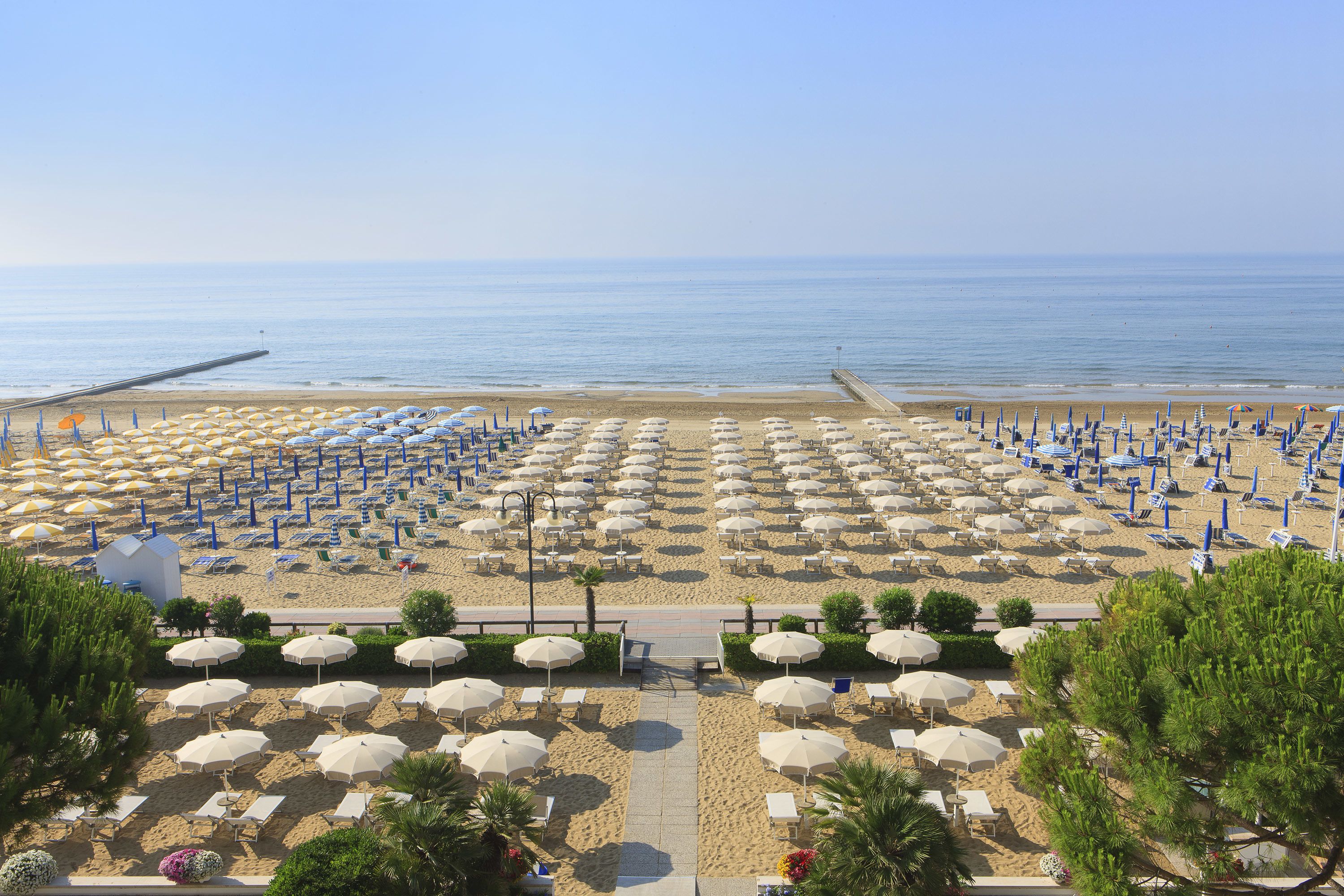 A beach with rows of umbrellas and sun loungers, a pier extending into the water, and a clear view of the sea.
