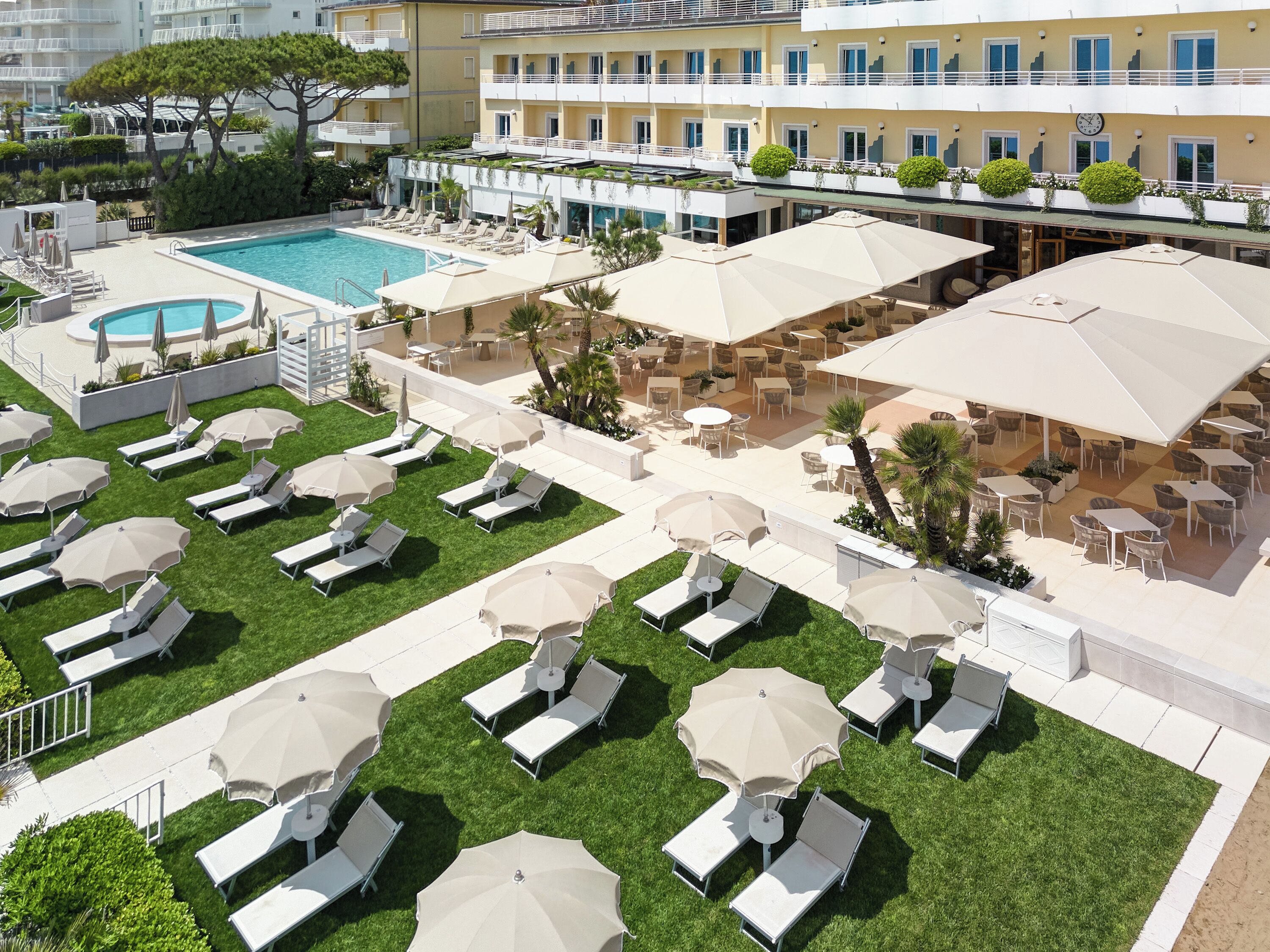 A rooftop pool area with sun loungers and umbrellas, surrounded by a building with balconies and outdoor seating.