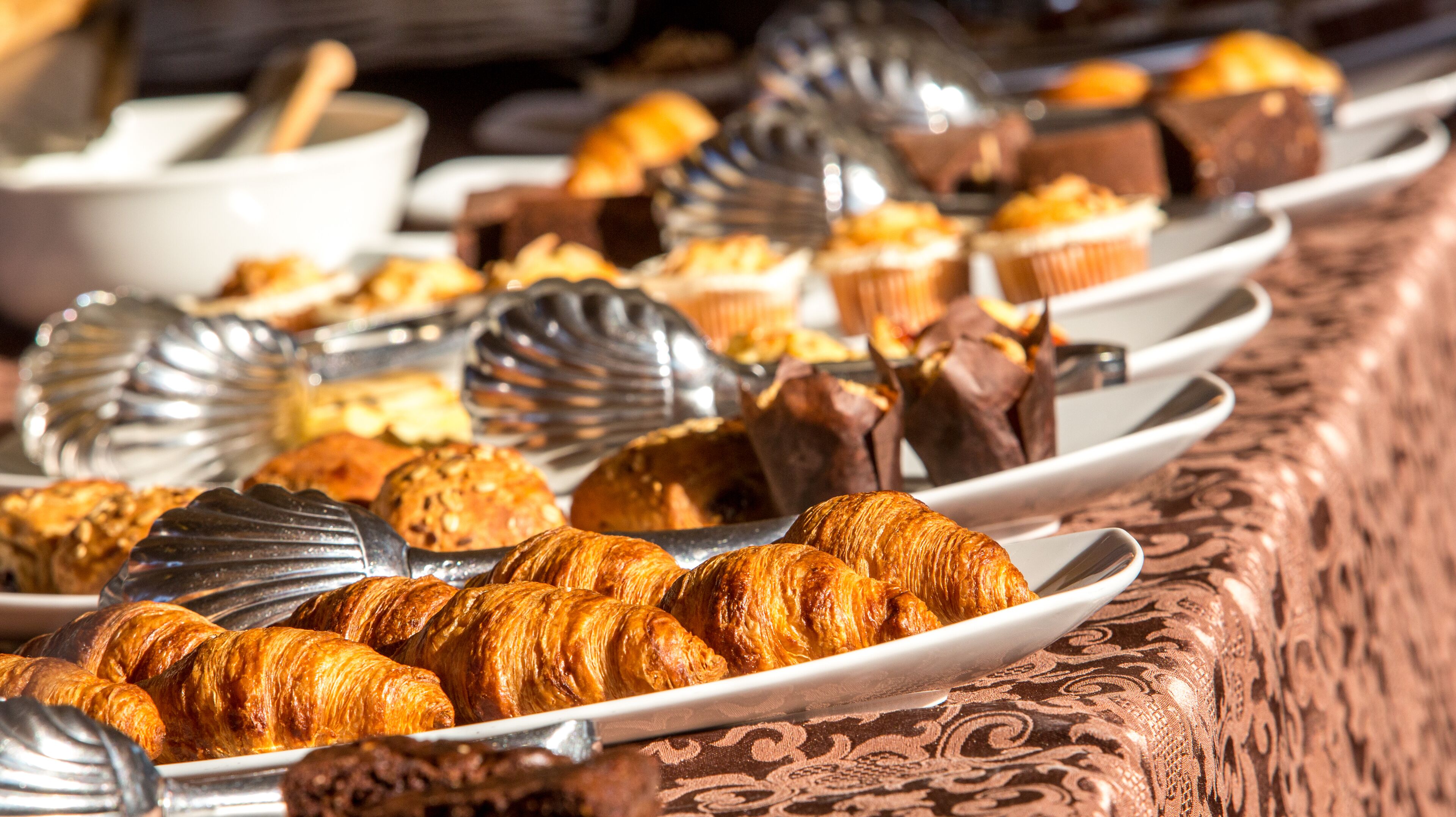 A buffet with various pastries and desserts, including croissants and chocolate items, arranged on plates.