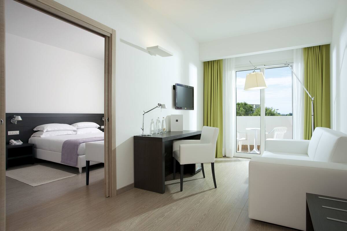 A hotel room with a bed, desk, chair, and a balcony with a view.