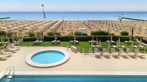 A pool area with a view of the beach, lounge chairs, and umbrellas.