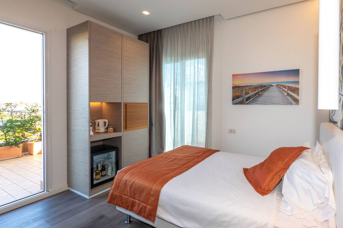 A modern hotel room with a bed, a built-in wardrobe, a television, and a large window with a view of the outdoors.