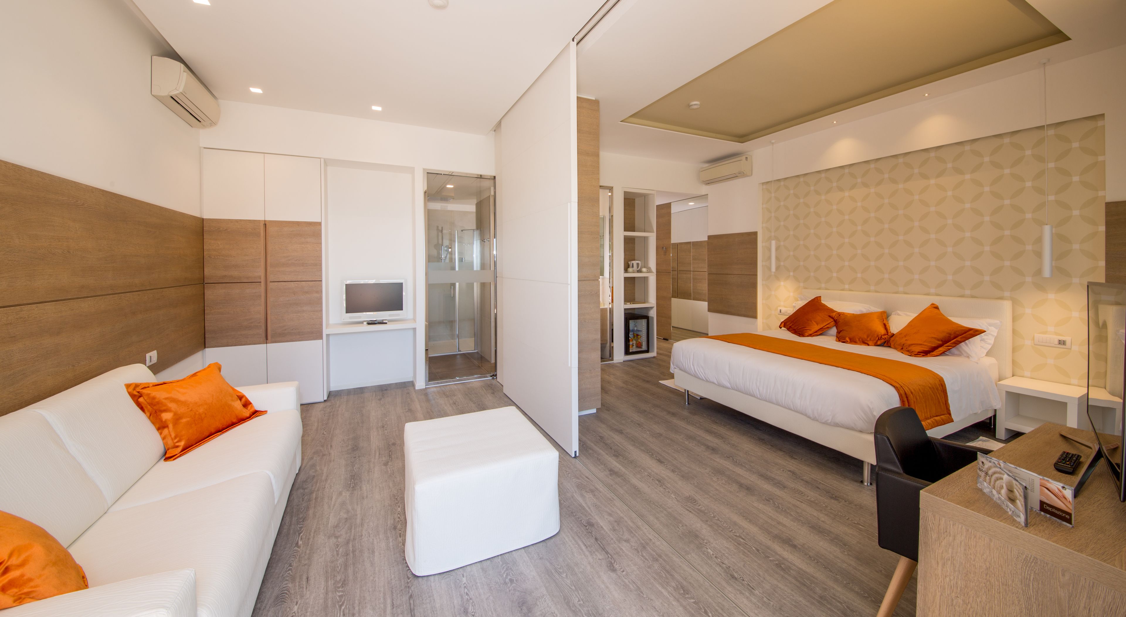 A modern hotel room with a sofa, two beds, a TV, a desk, and a bathroom.