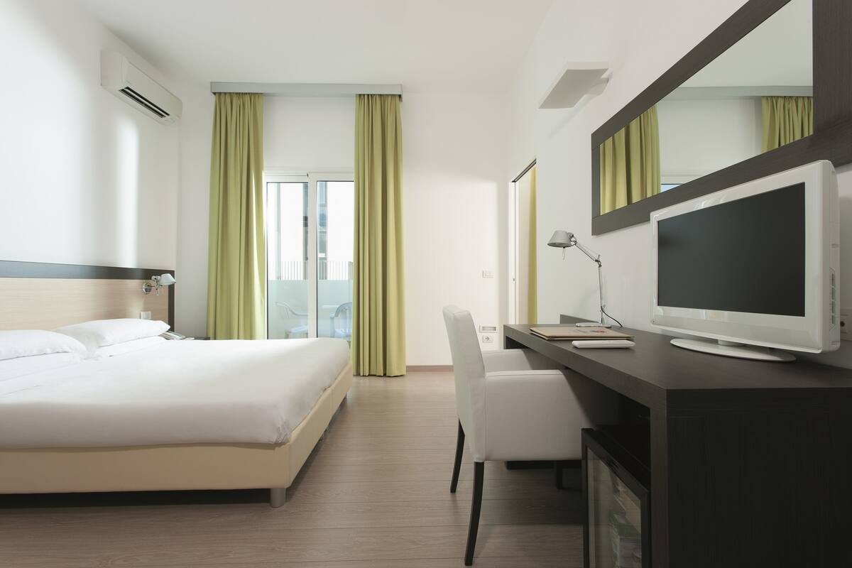 A hotel room with a bed, a desk with a computer, a television, and a mirror.