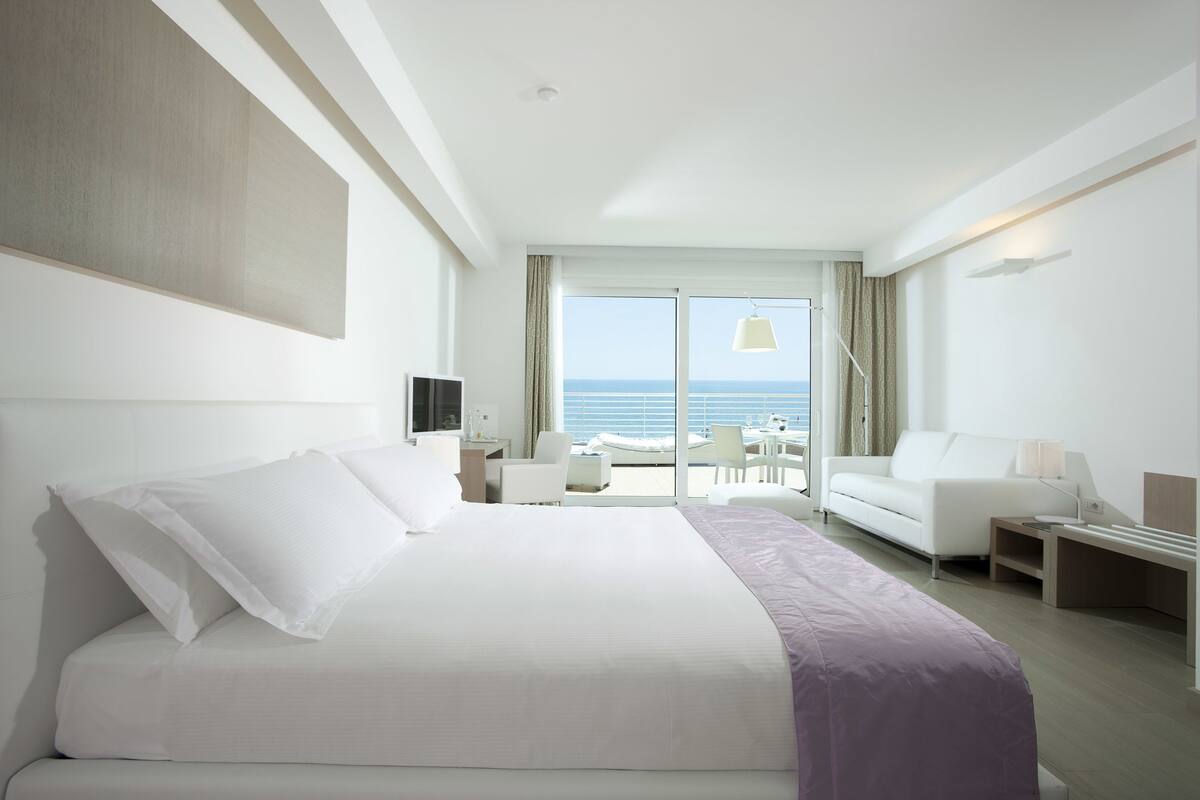 A hotel room with a large bed, a sofa, a desk, and a view of the sea.