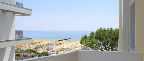 A balcony with a view of a beach, a table with a book, and a chair.