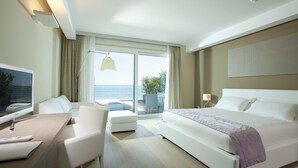 A modern hotel room with a bed, a desk with a computer, a chair, and a view of the outdoors.