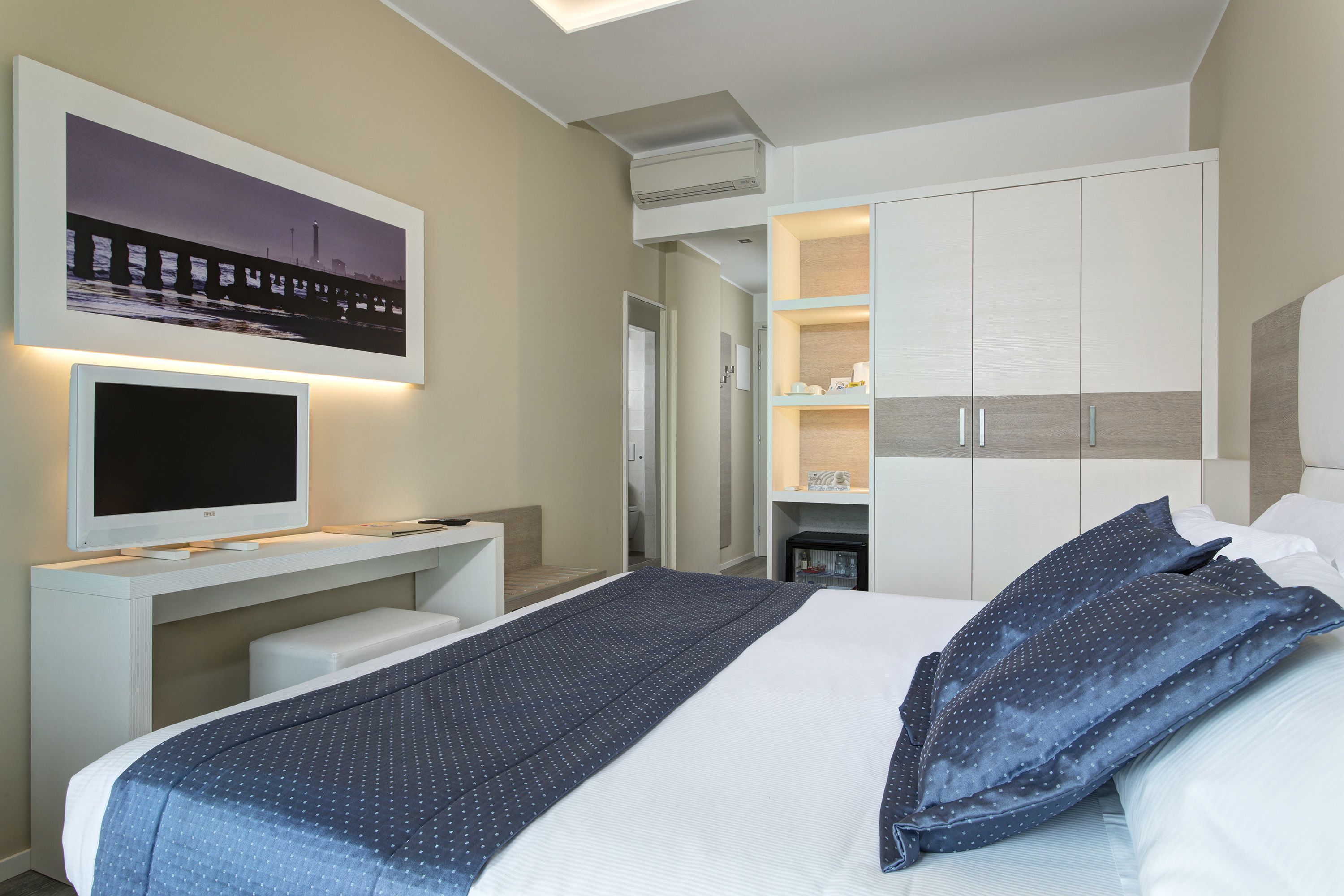 A modern hotel room with a bed, a TV, a desk, and a wardrobe.