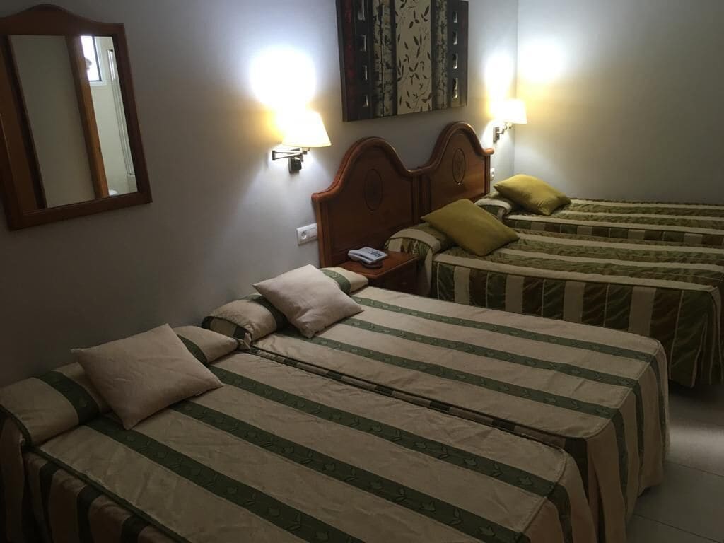 A hotel room with two single beds, each with a wooden headboard, a nightstand, and a wall-mounted lamp.