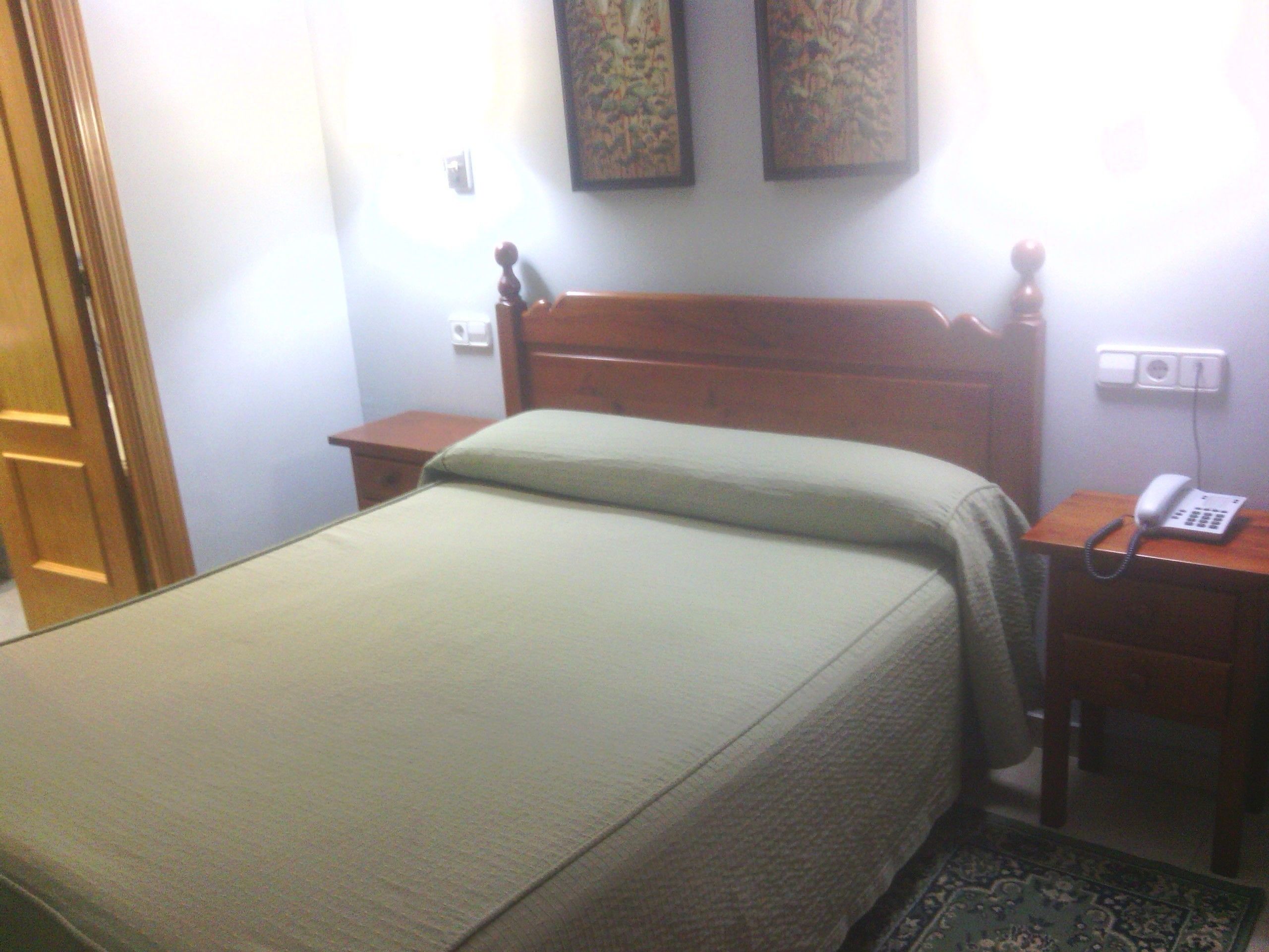 A simple room with a bed, a bedside table with a telephone, and a nightstand.