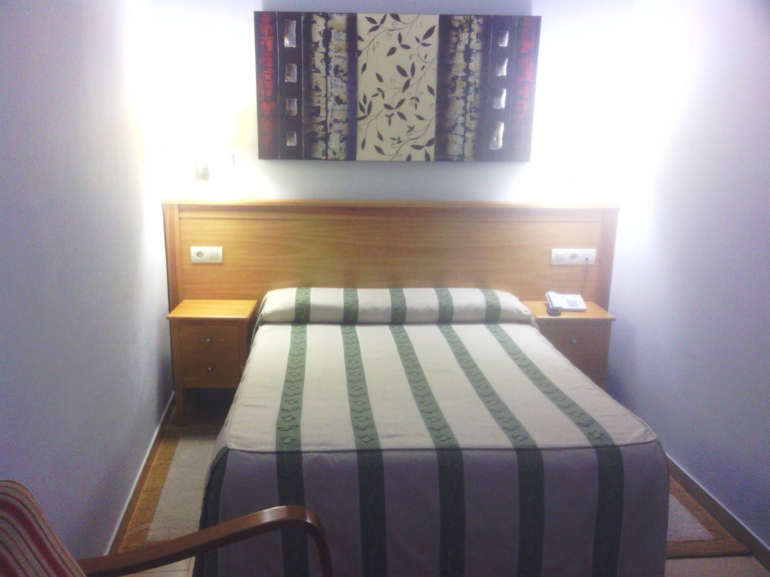 A hotel room with a wooden headboard, a bed with striped bedding, a nightstand with a phone, and a wall-mounted artwork.
