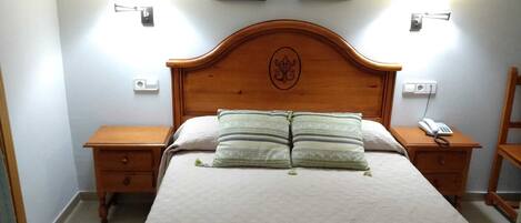 A neatly made bed with a wooden headboard, two bedside tables, and a wall-mounted telephone.