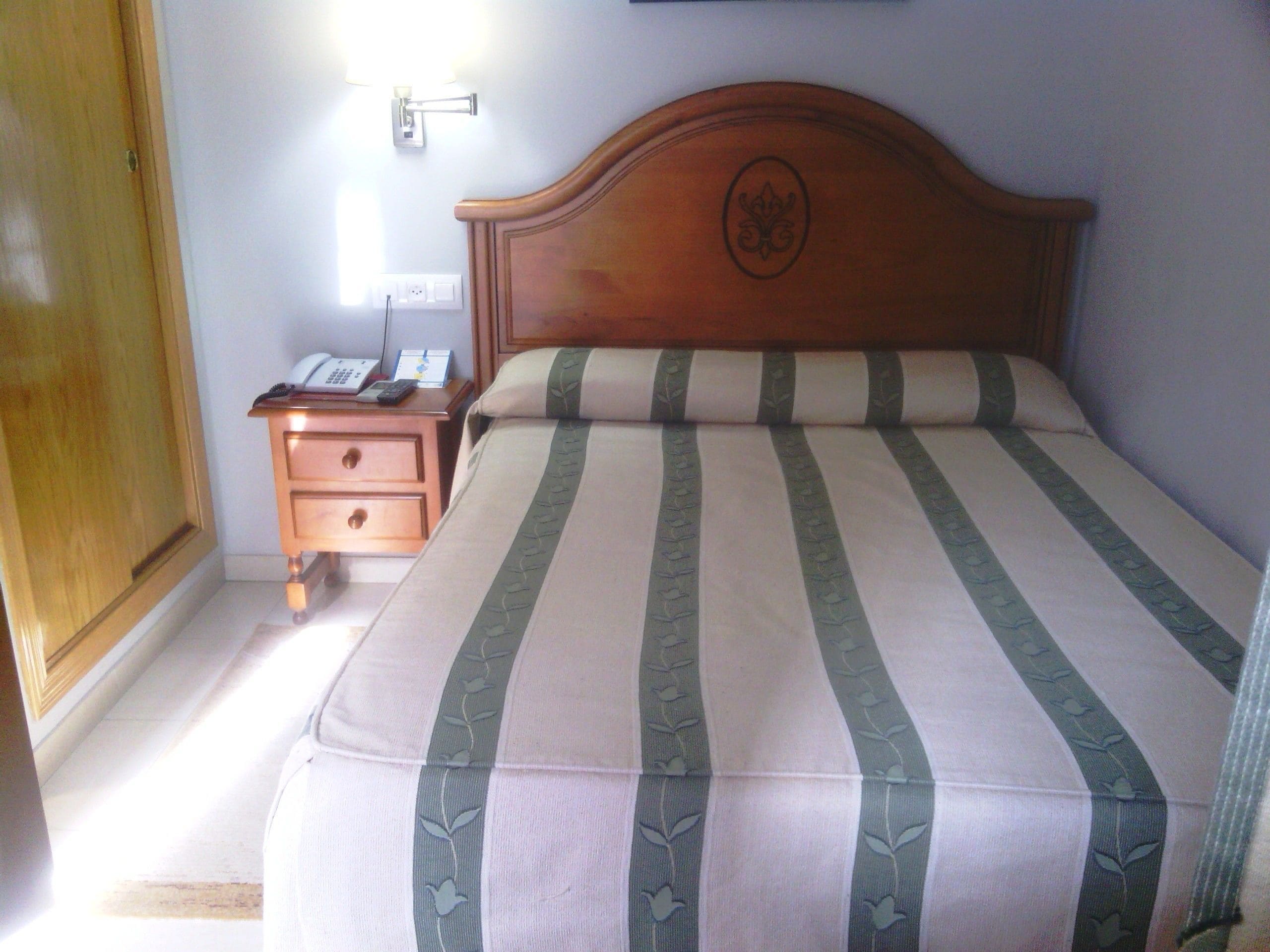 A neatly made bed with a striped bedspread, a wooden headboard, and a bedside table with a lamp and a phone.
