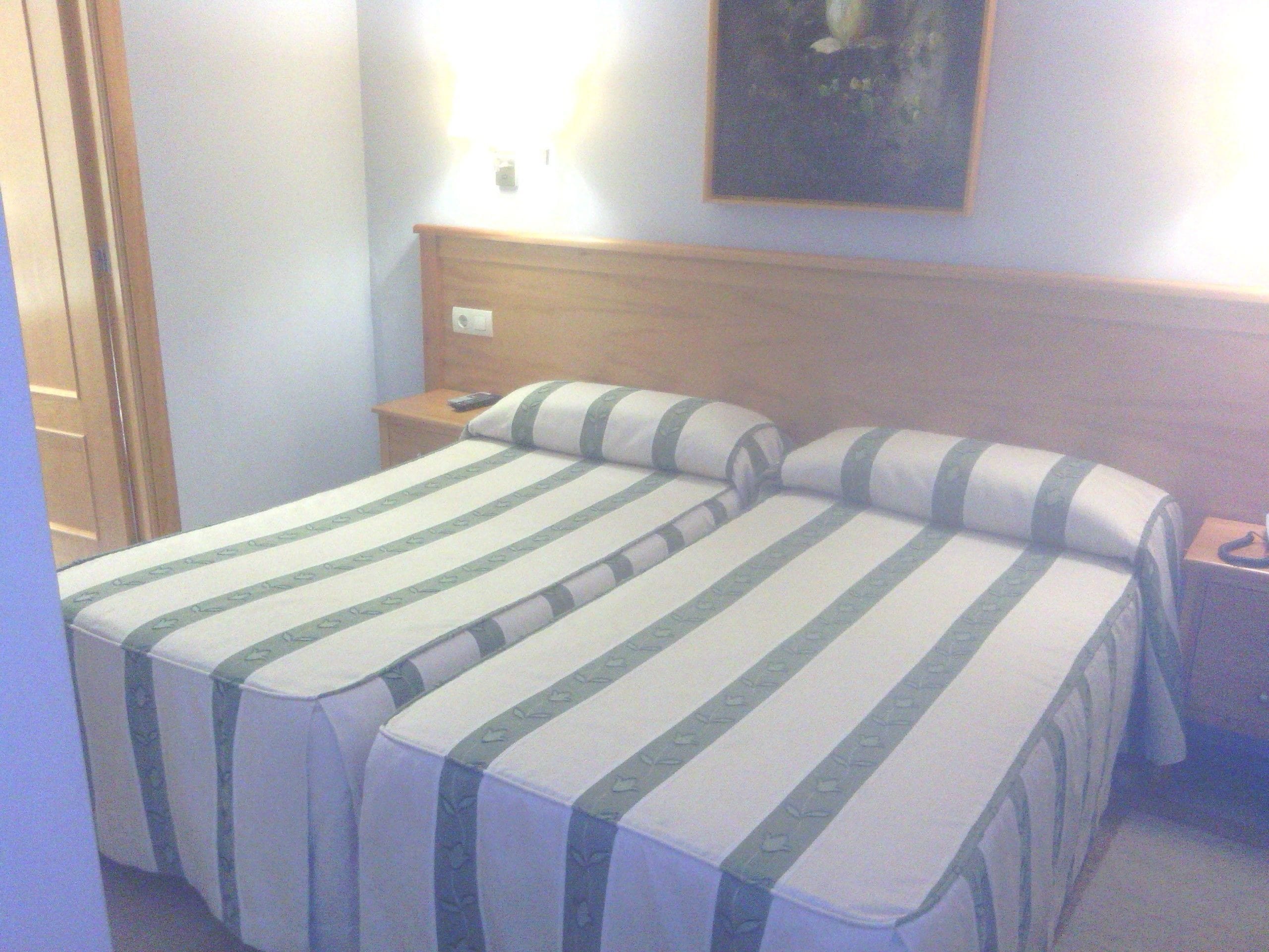 A hotel room with two beds, a wooden headboard, a nightstand, and a painting on the wall.
