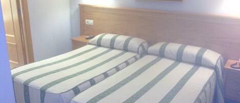 A hotel room with two beds, a wooden headboard, a nightstand, and a painting on the wall.