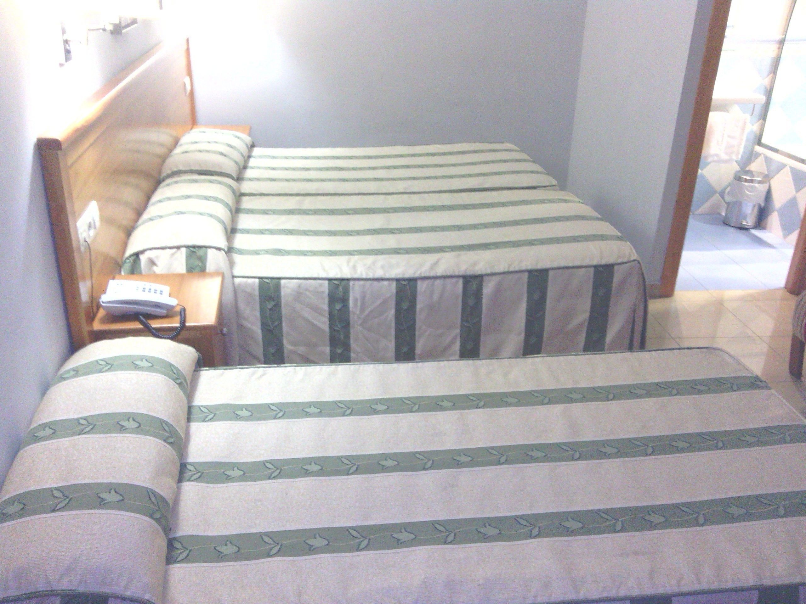 A double bed with striped bedding, a bedside table with a phone, and a window with a view of the outside.