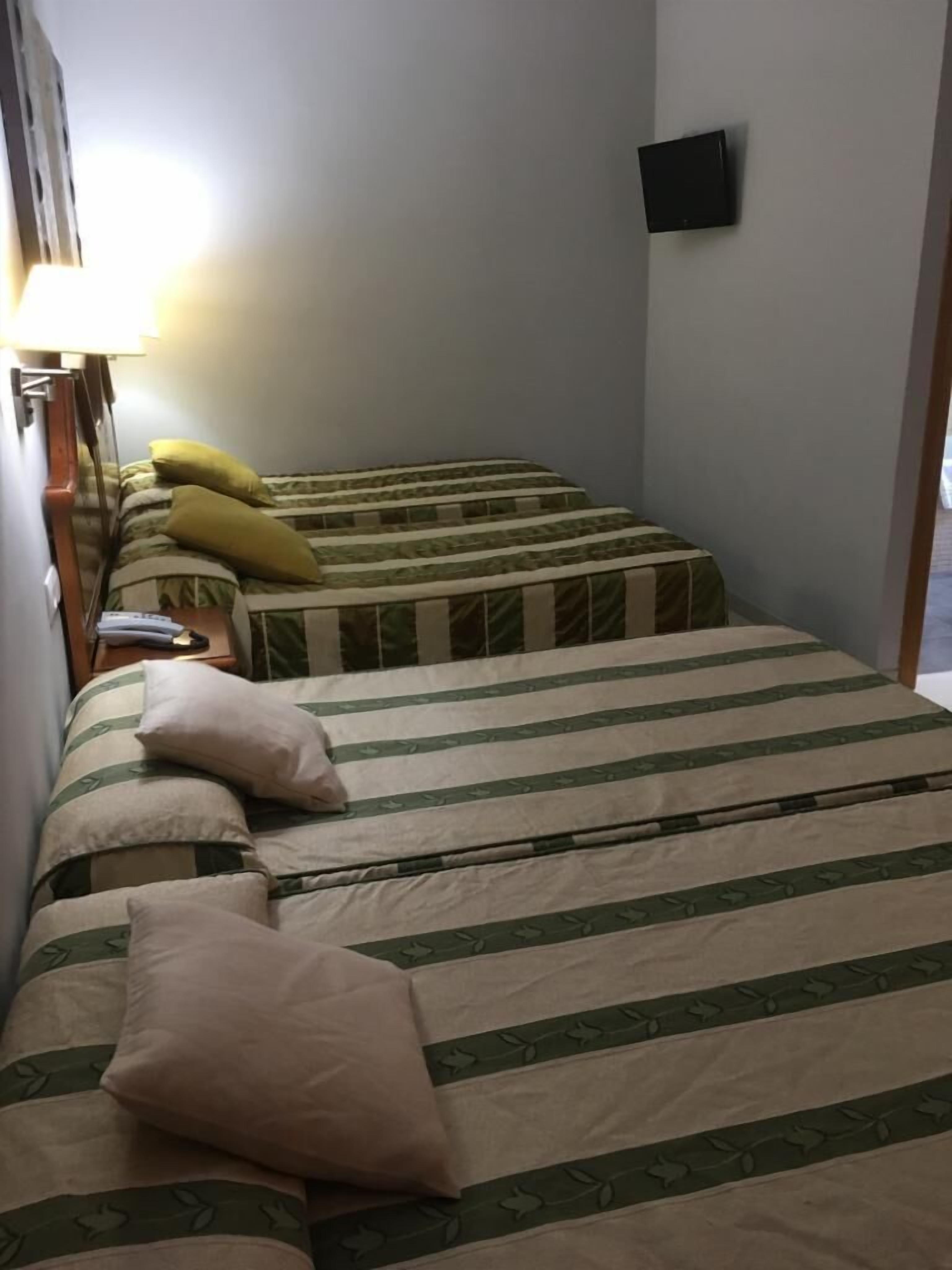 Habitación de hotel con dos camas, cada una con ropa de cama y almohadas a rayas. Un televisor de pantalla plana está montado en la pared.