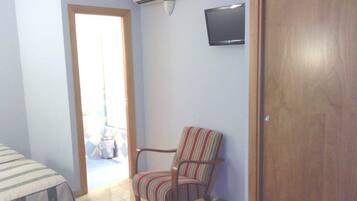 Ein Zimmer mit Holztür, einem gestreiften Sessel, einem an der Wand befestigten Fernseher und einer Klimaanlage.