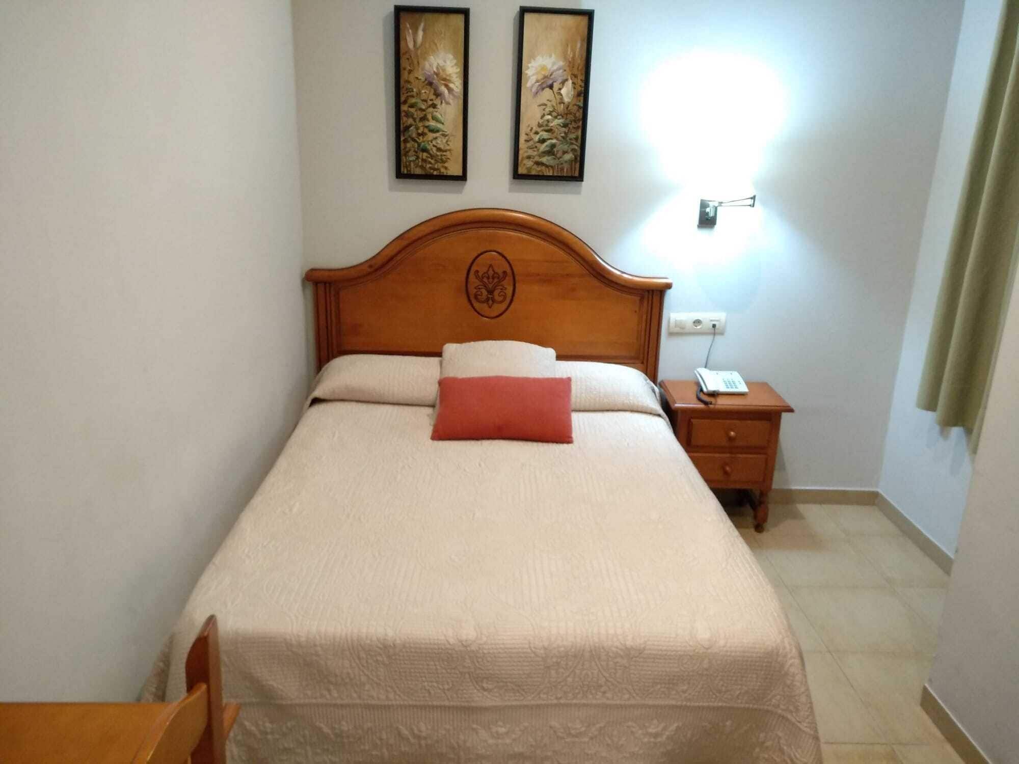 Uma cama bem arrumada com cabeceira de madeira, mesa de cabeceira com um telefone e dois quadros florais emoldurados na parede.