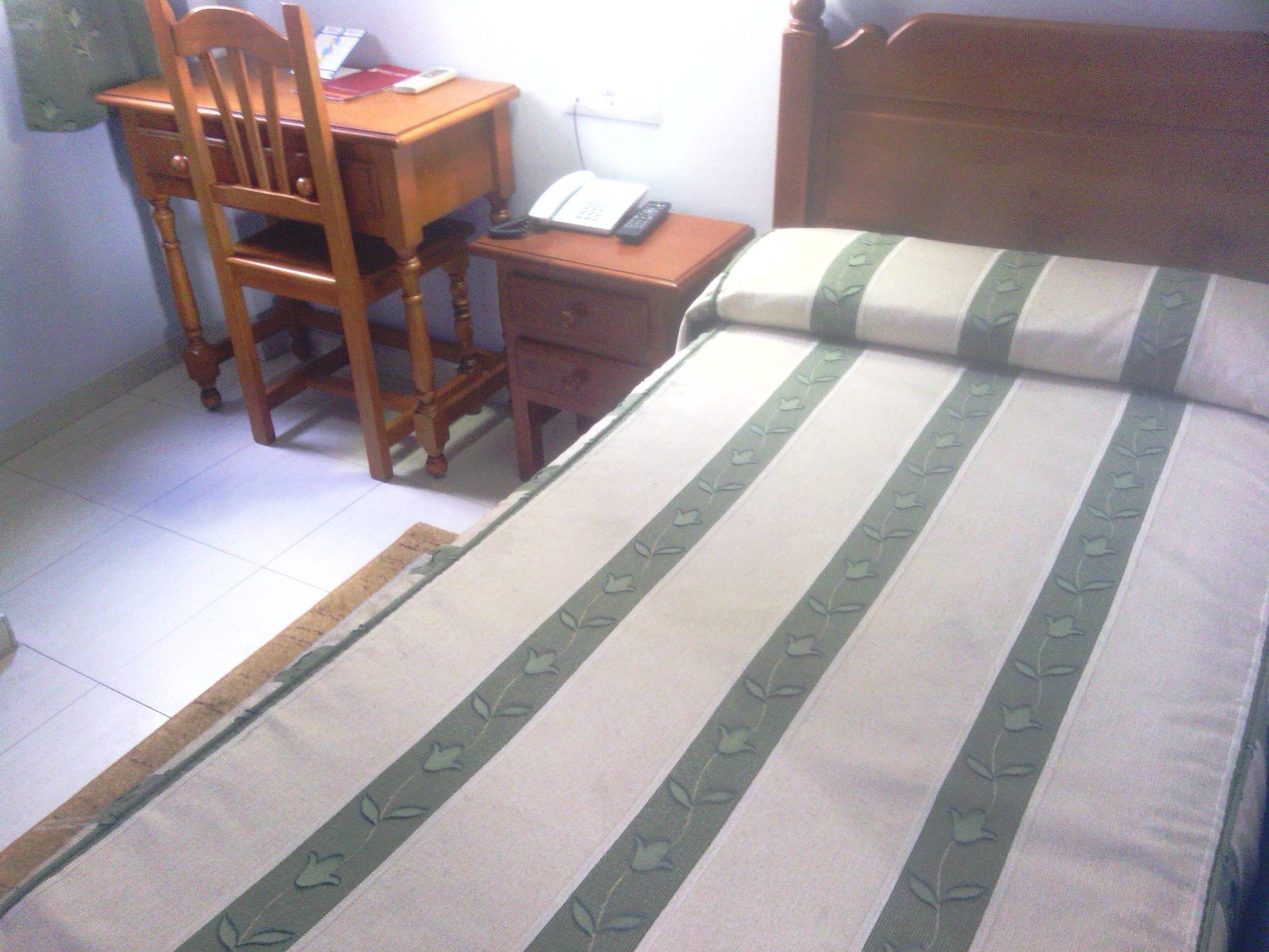 Ein Schlafzimmer mit einem Bett, einem Holzsessel, einem Nachttisch und einem Schreibtisch.