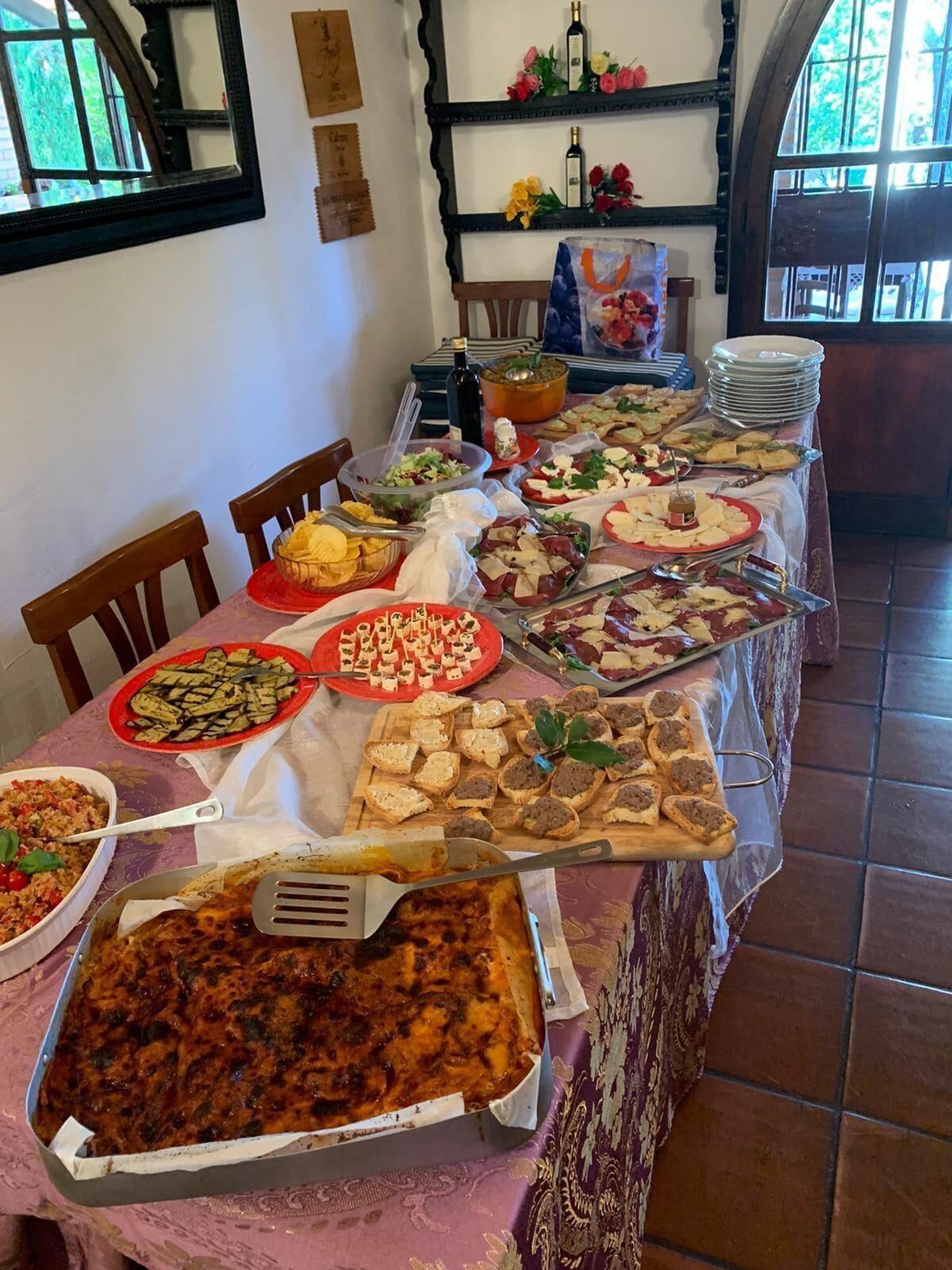 A dining table with various dishes, including a large lasagna, salads, and bread.