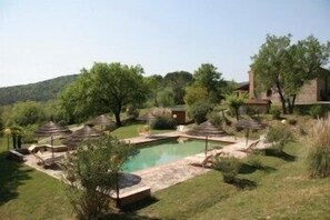 Un espace piscine avec un jacuzzi, entouré d’arbres et avec un bâtiment en arrière-plan.