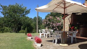 Un patio con mesa y sillas, rodeado de plantas en macetas y un muro de piedra.