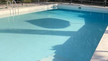 A rectangular swimming pool with clear blue water, surrounded by a tiled deck and a metal fence.