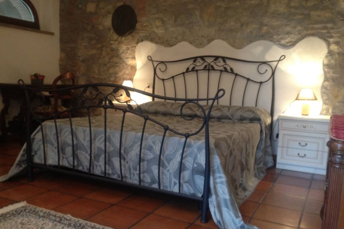 A bedroom with a metal bed frame, a bedside table with a lamp, a nightstand, and a patterned rug on the floor.