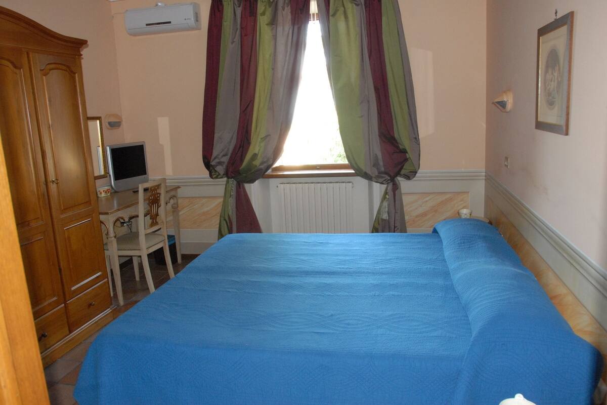 Une pièce comprenant un lit, un bureau avec un ordinateur, une chaise et une fenêtre avec des rideaux.
