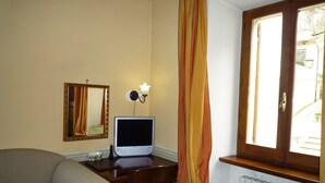 A hotel room with a bed, a desk with a computer, a chair, a mirror, and a window with curtains. - Il Panciolle (Spoleto)