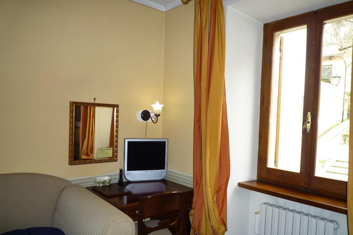 Une chambre d’hôtel avec un lit, un bureau équipé d’un ordinateur, une chaise, un miroir et une fenêtre avec des rideaux.