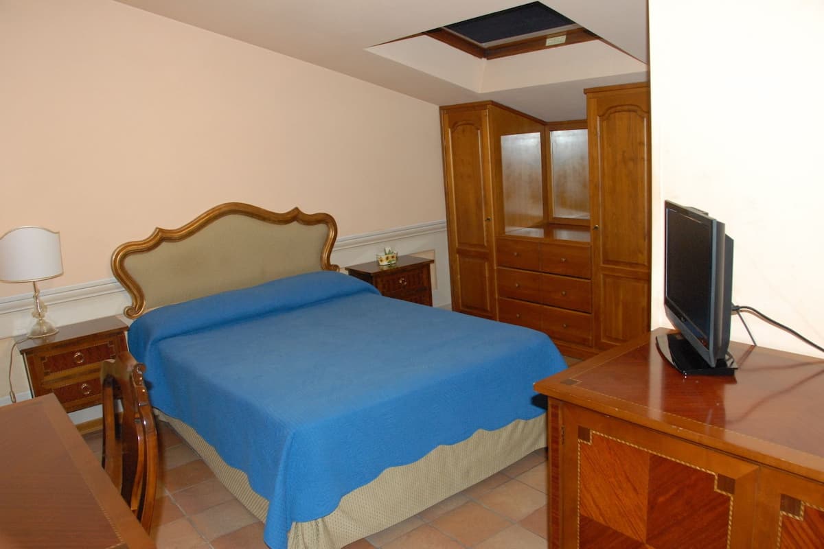 Une chambre à coucher comprenant un lit, une armoire en bois, un bureau avec une télévision et une table de chevet avec une lampe.