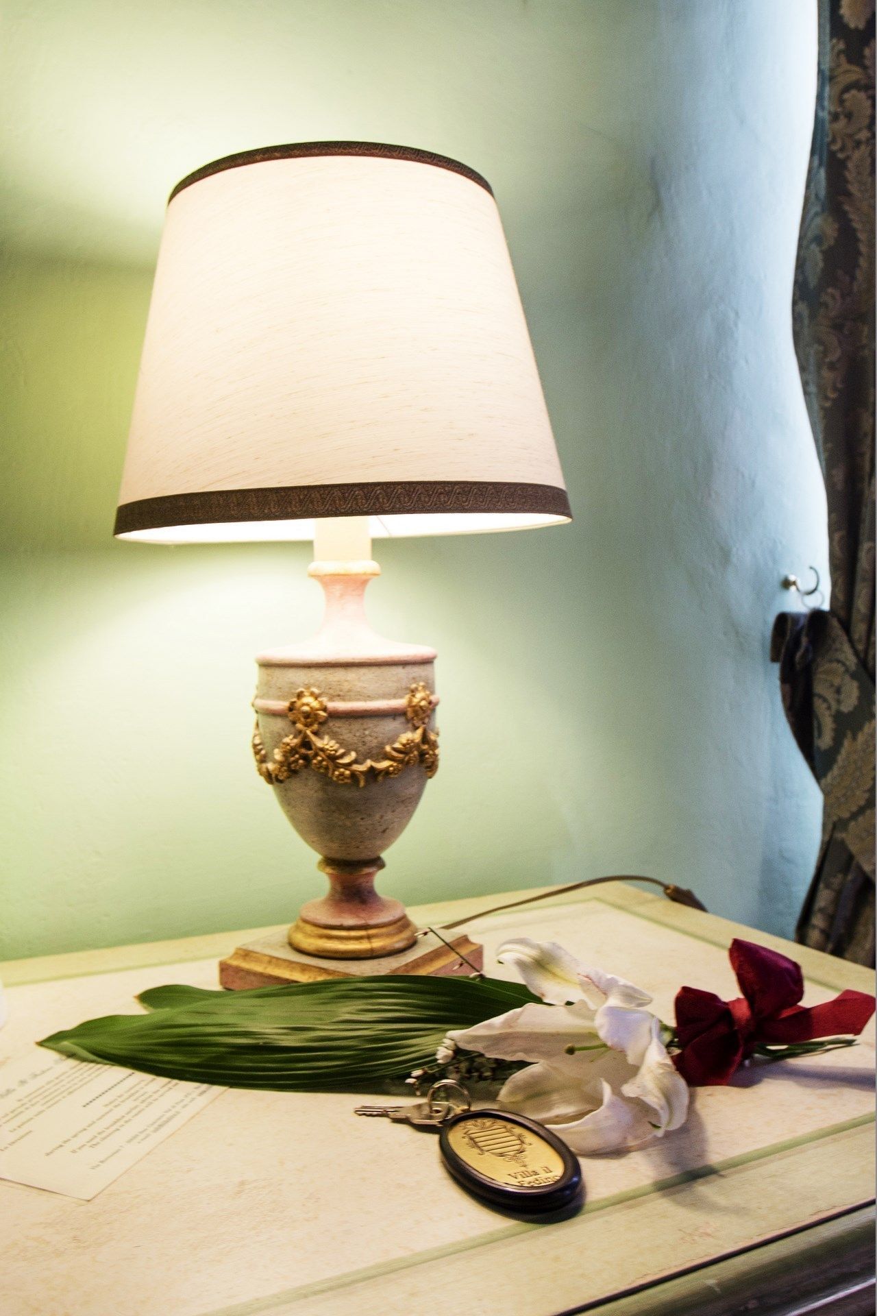 A table with a lamp, a keychain, a white flower, and a red flower on a tablecloth.