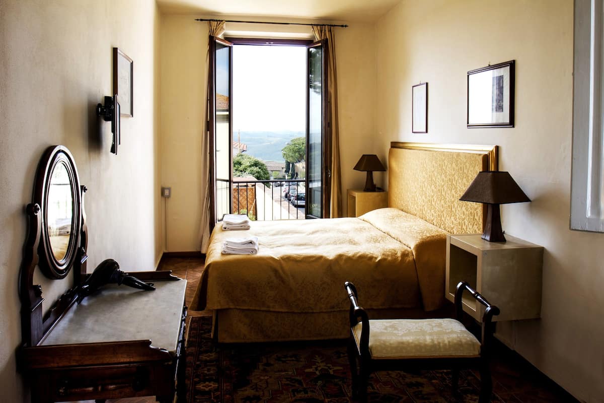 Une chambre d’hôtel équipée d’un lit, d’une chaise, d’un bureau, d’un miroir, d’une lampe et offrant une vue sur l’extérieur.