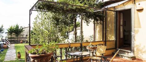 A balcony with a pergola, potted plants, a table, and chairs.