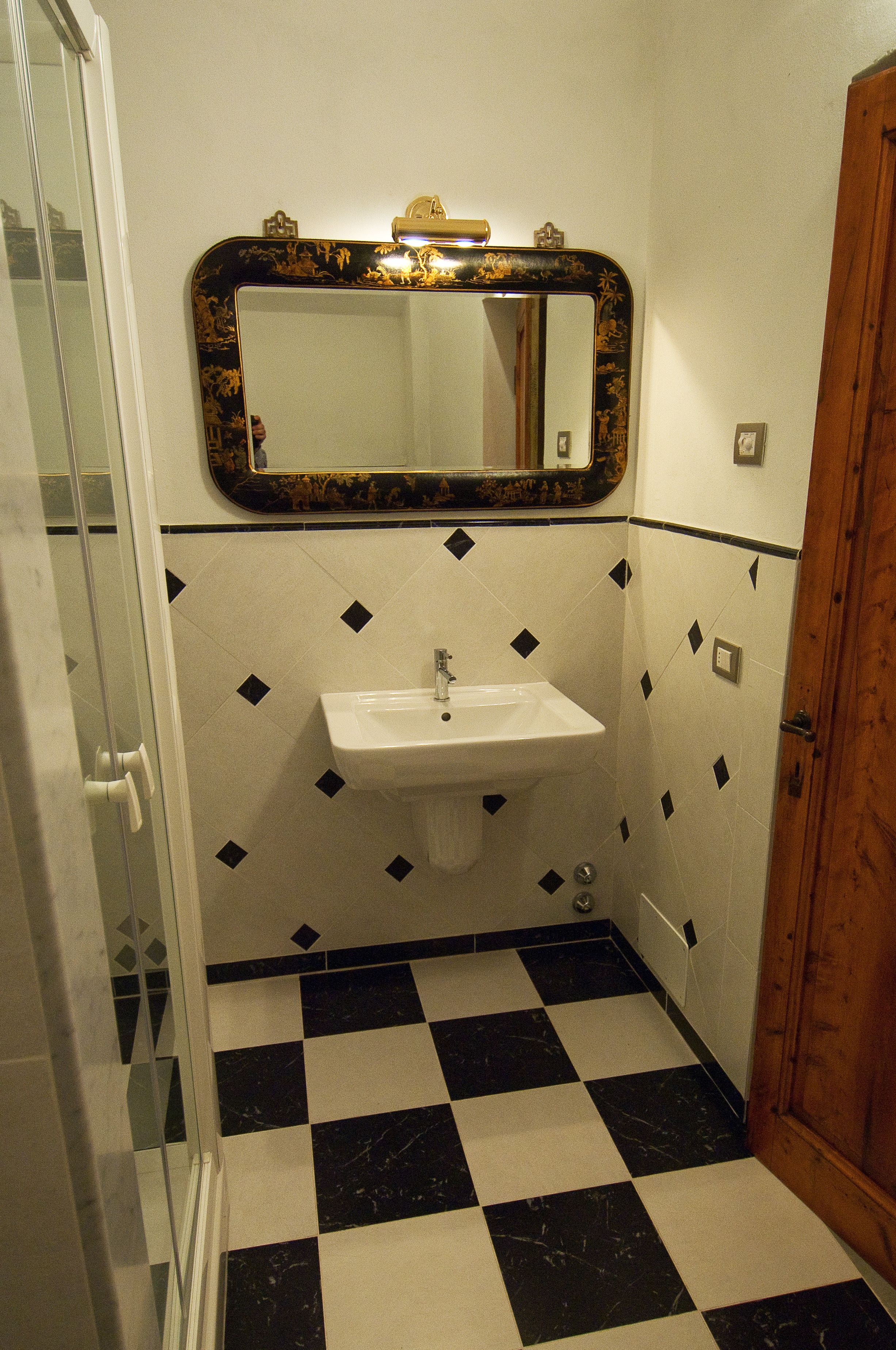 A bathroom with a checkered floor, a sink, and a mirror with a decorative frame.